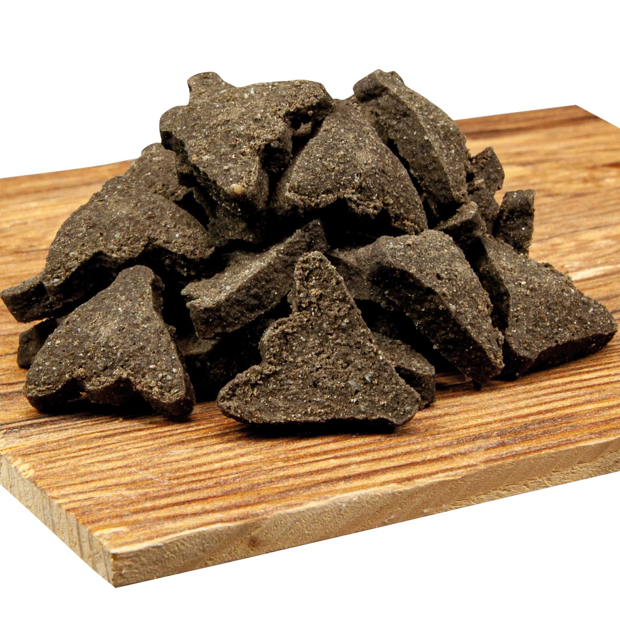 Hundeleckerlis in Herzform auf Holzbrett. Dunkle Farbe, grobe Textur. Gehäuft angeordnet.