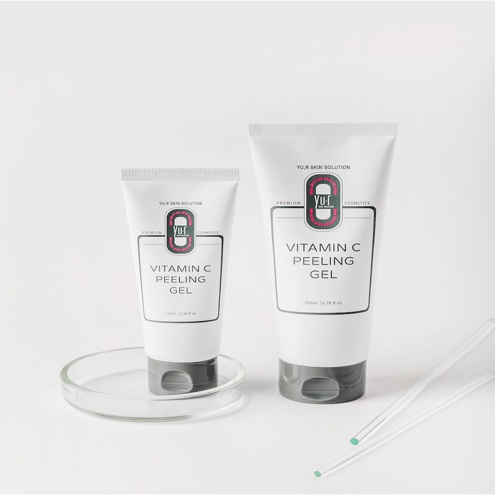 Zwei Tuben Vitamin C Peeling Gel, eine kleine und eine große, mit grauen Kappen. Auf einer Glasplatte.
