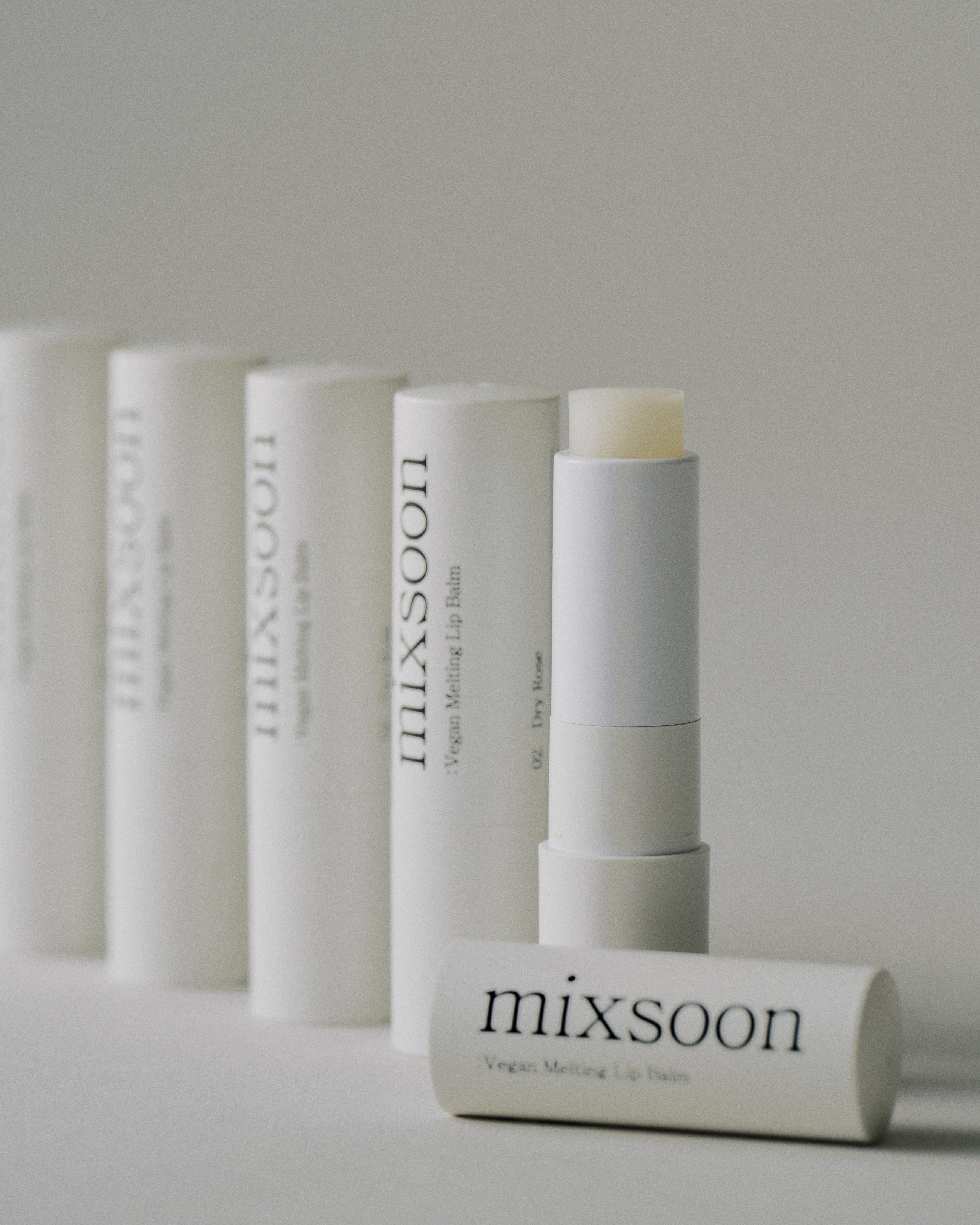 Mehrere weiße Lippenbalsam-Sticks und eine offene Kappe. Auf den Sticks steht "mixsoon Vegan Melting Lip Balm".