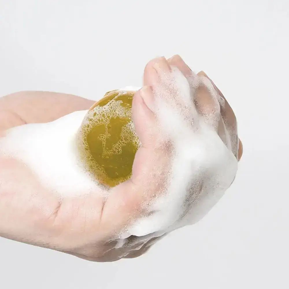 Hand hält gelbe Kugel mit Schaum bedeckt. Weißer Hintergrund.