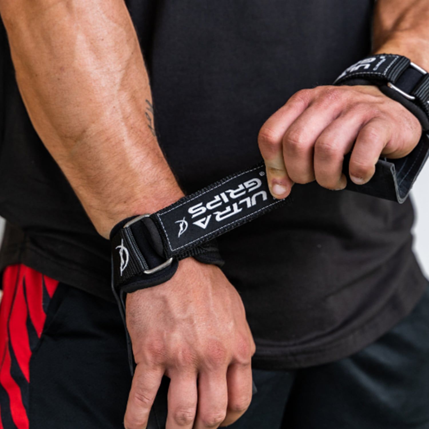Person hält Ultra-Grip am Handgelenk. Schwarzer Riemen mit "ULTRA GRIPS" Schriftzug.