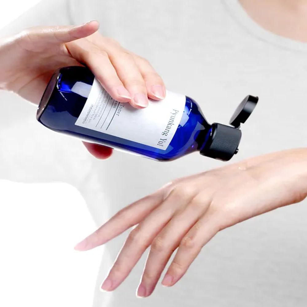Blaue Flasche wird über eine Hand gehalten. Schwarzer Deckel ist geöffnet. Flüssigkeit wird ausgegossen.
