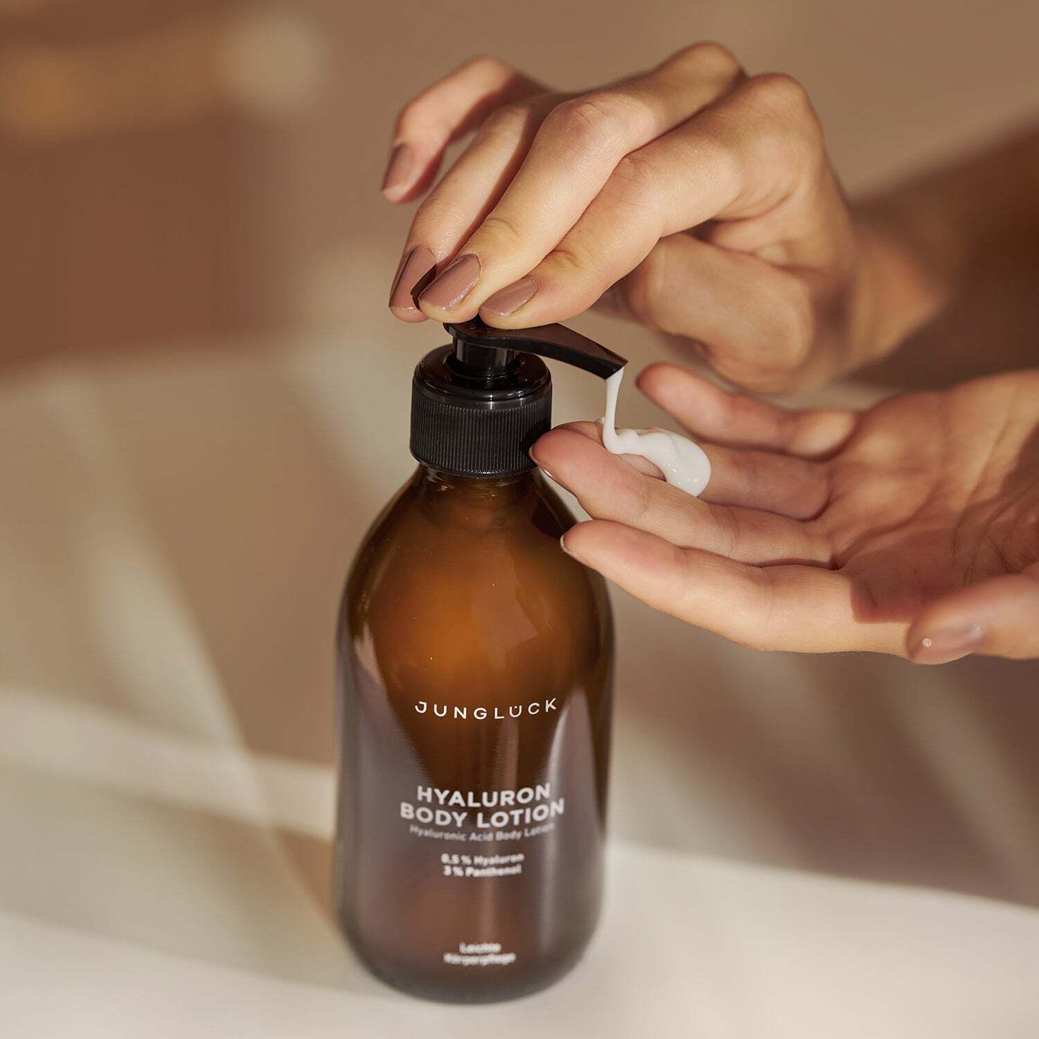 Hände drücken Lotion aus einer braunen Flasche mit schwarzem Pumpkopf. Lotion wird auf die Handfläche gegeben.