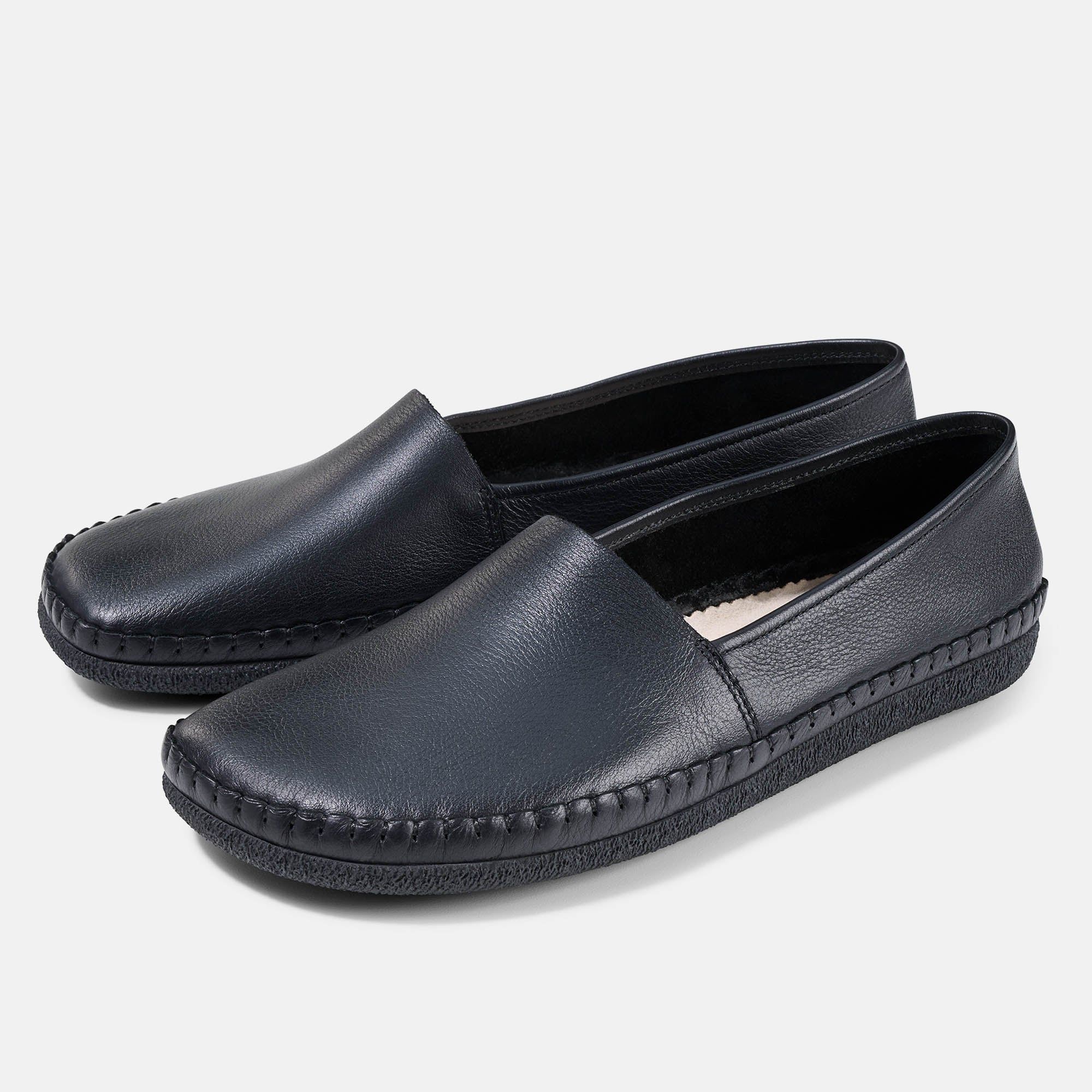 Zwei schwarze Unisex-Slipper mit breiter Passform. Glattes Leder, quadratische Zehenpartie, sichtbare Nähte an der Sohle.