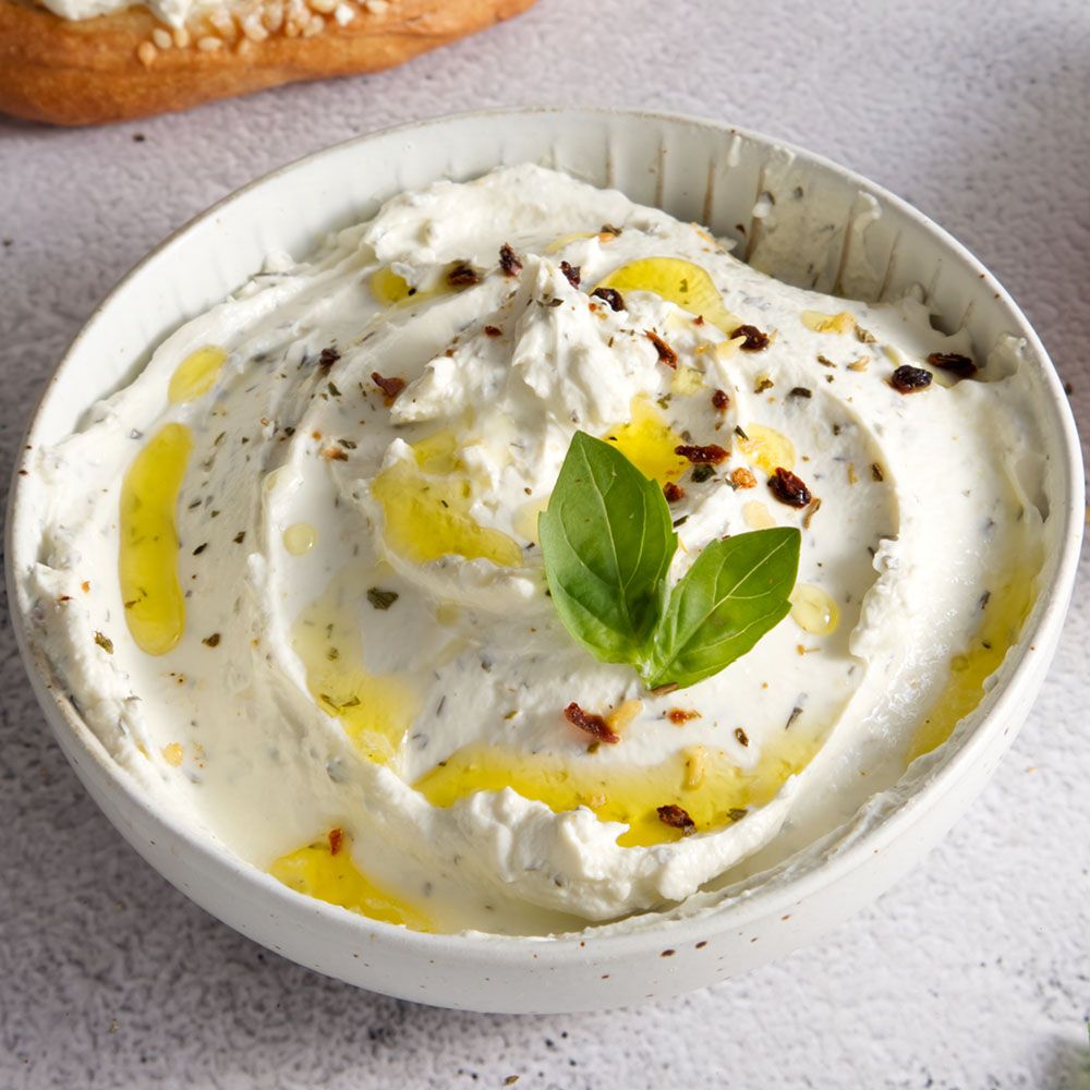 Schüssel mit Frischkäse, garniert mit Olivenöl und Basilikum. Nahaufnahme. Helle Oberfläche.