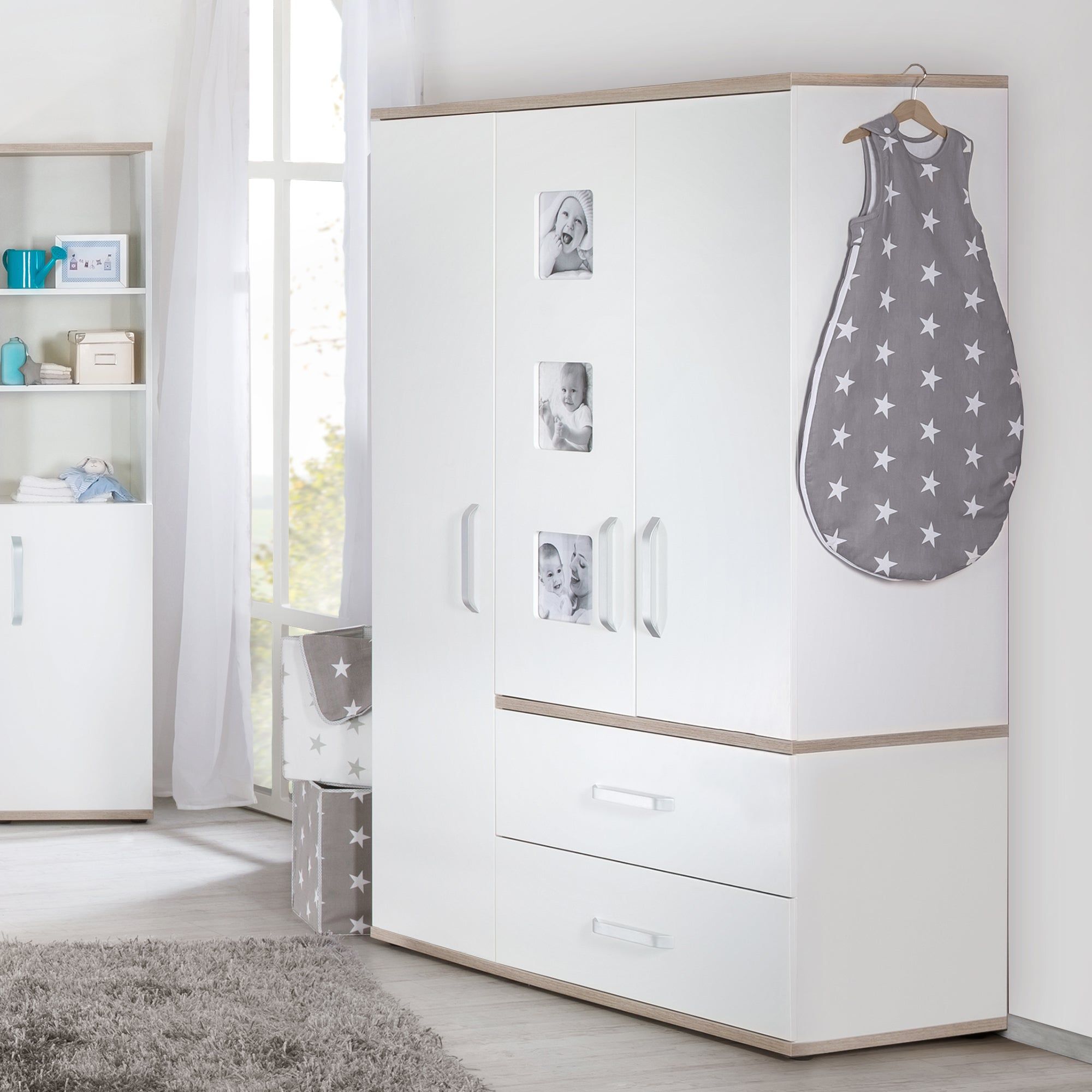 Babyschlafsack "Little Stars" an Kleiderhaken. Grau mit weißen Sternen. Hängt an einem weißen Schrank mit Fotos.