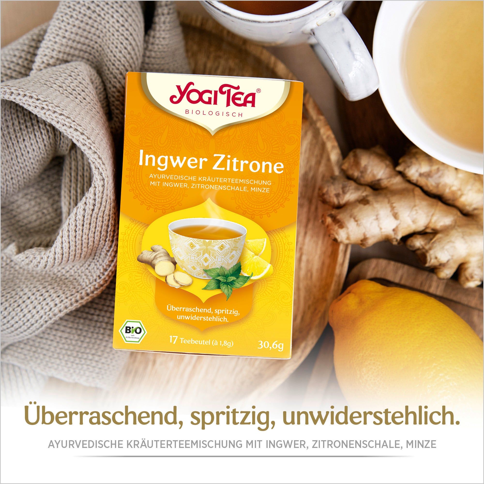 Yogi Tea Ingwer Zitrone Packung auf Holztablett. Ingwer, Zitrone und Tasse Tee daneben. Text: Überraschend, spritzig, unwiderstehlich.