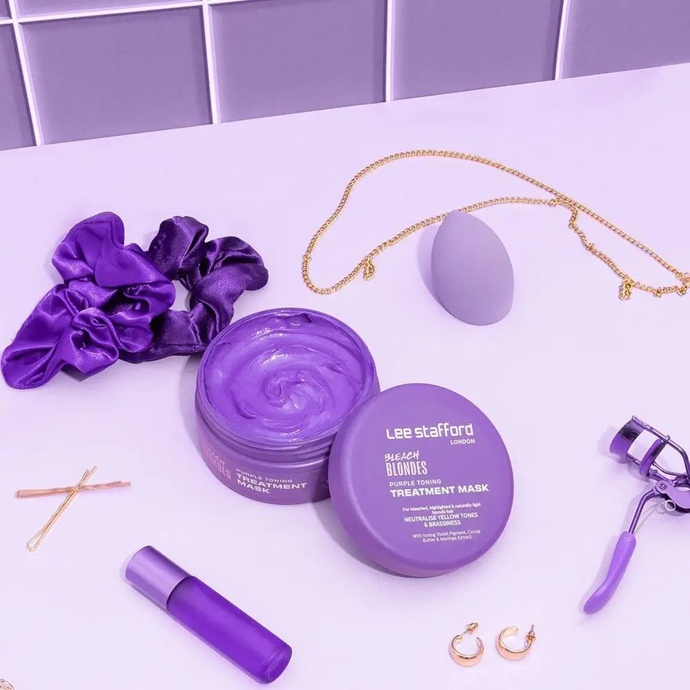 Zwei offene lila Tiegel, Haargummi, Schmuck, Wimpernzange, Make-up-Schwamm, Haarnadeln und Ohrringe.