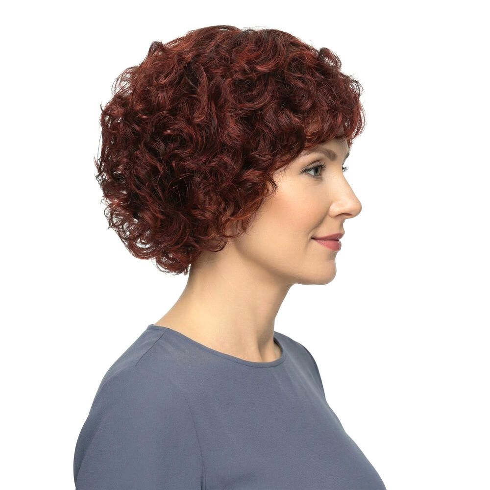 Frau mit roter, lockiger Perücke. Seitenansicht. Kurzes, voluminöses Haar. Bluse in Blau. Weißer Hintergrund.