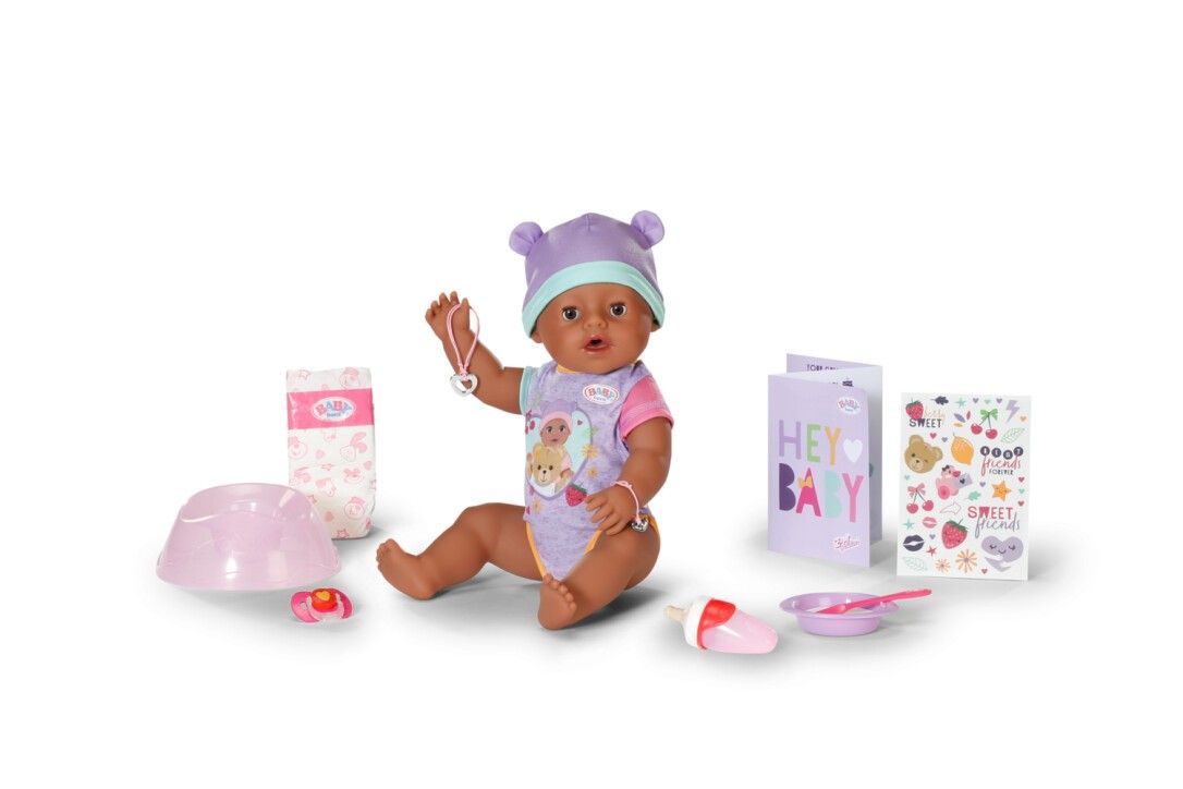 Puppe mit lila Mütze und Strampler. Zubehör: Windel, Teller, Löffel, Flasche, Karte und Aufkleber. Puppe hält Kette.