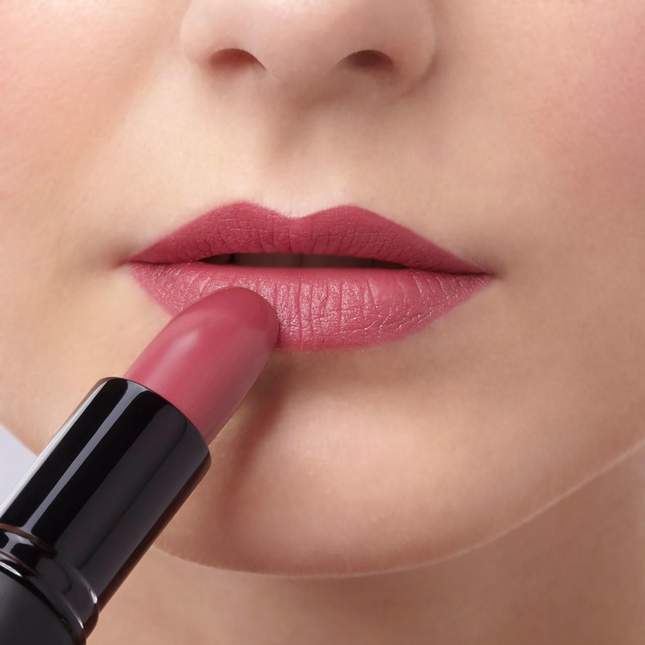 Lippen, die mit einem rosafarbenen Lippenstift geschminkt werden. Nahaufnahme.