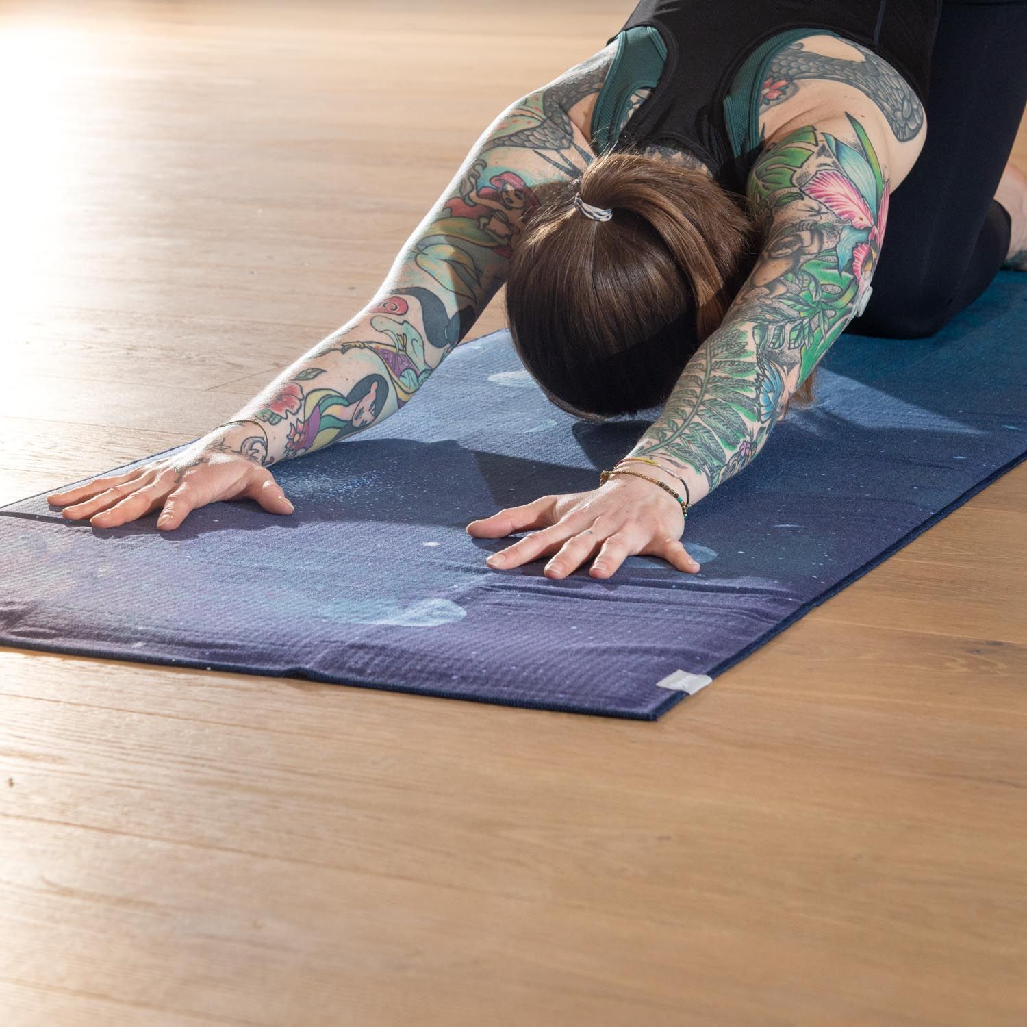 Person in Yoga-Position auf Yoga-Tuch, nightblue, mit Mond-Design. Auf Holzboden.