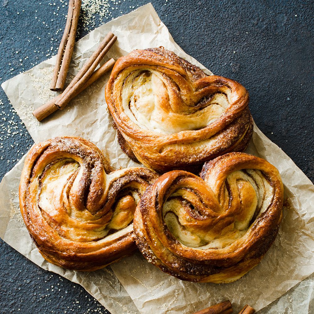 Franzbrötchen auf Papier. Zimtstangen daneben. Draufsicht auf dunklem Untergrund. Zucker gestreut.