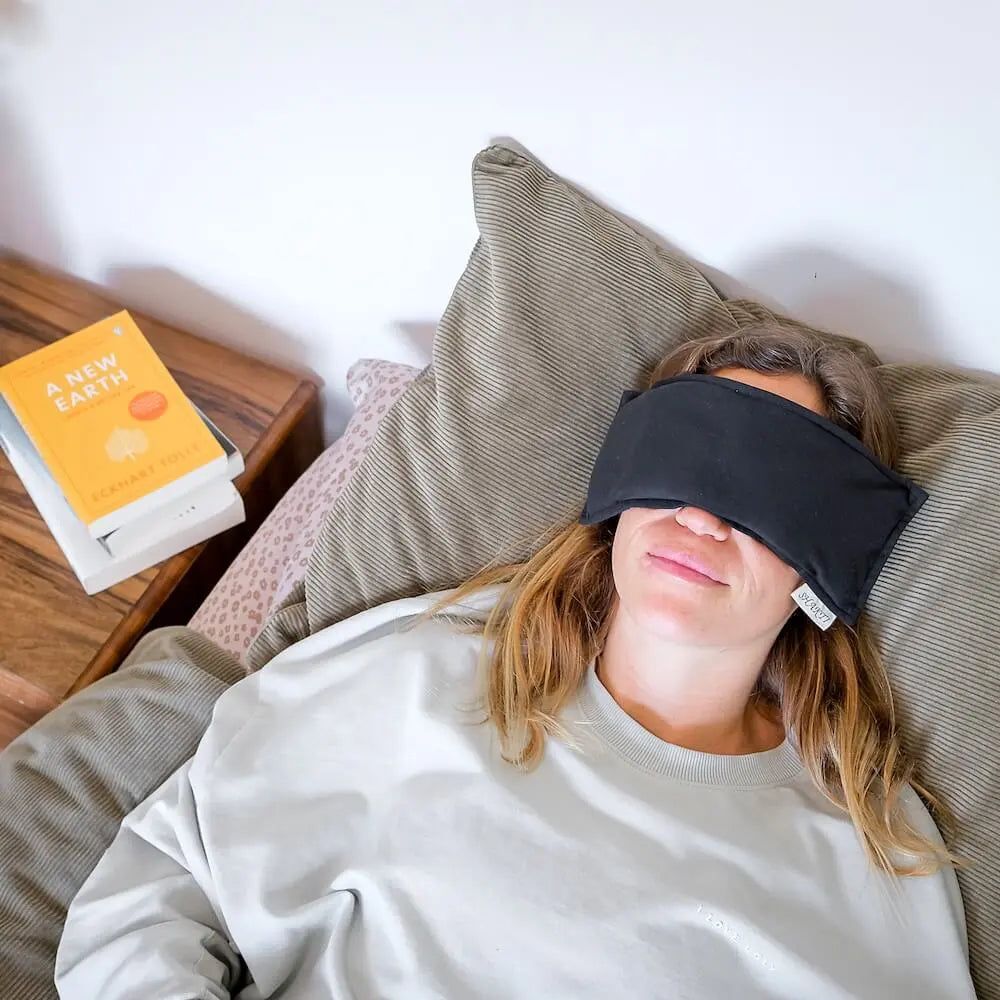 Frau mit schwarzem Augenkissen auf den Augen, liegend auf einem Bett.