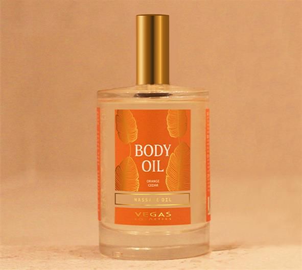 Körperöl-Flasche mit goldfarbenem Verschluss. Etikett mit Schriftzug "BODY OIL" und "Orange Cedar". Marke: Vegas Cosmetics.
