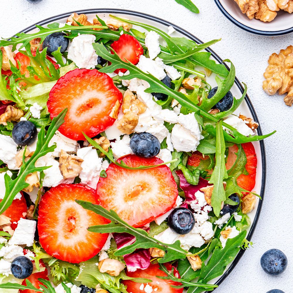 Salat mit Erdbeeren, Blaubeeren, Walnüssen und Käse. Auf einem Teller mit grünem Salat.