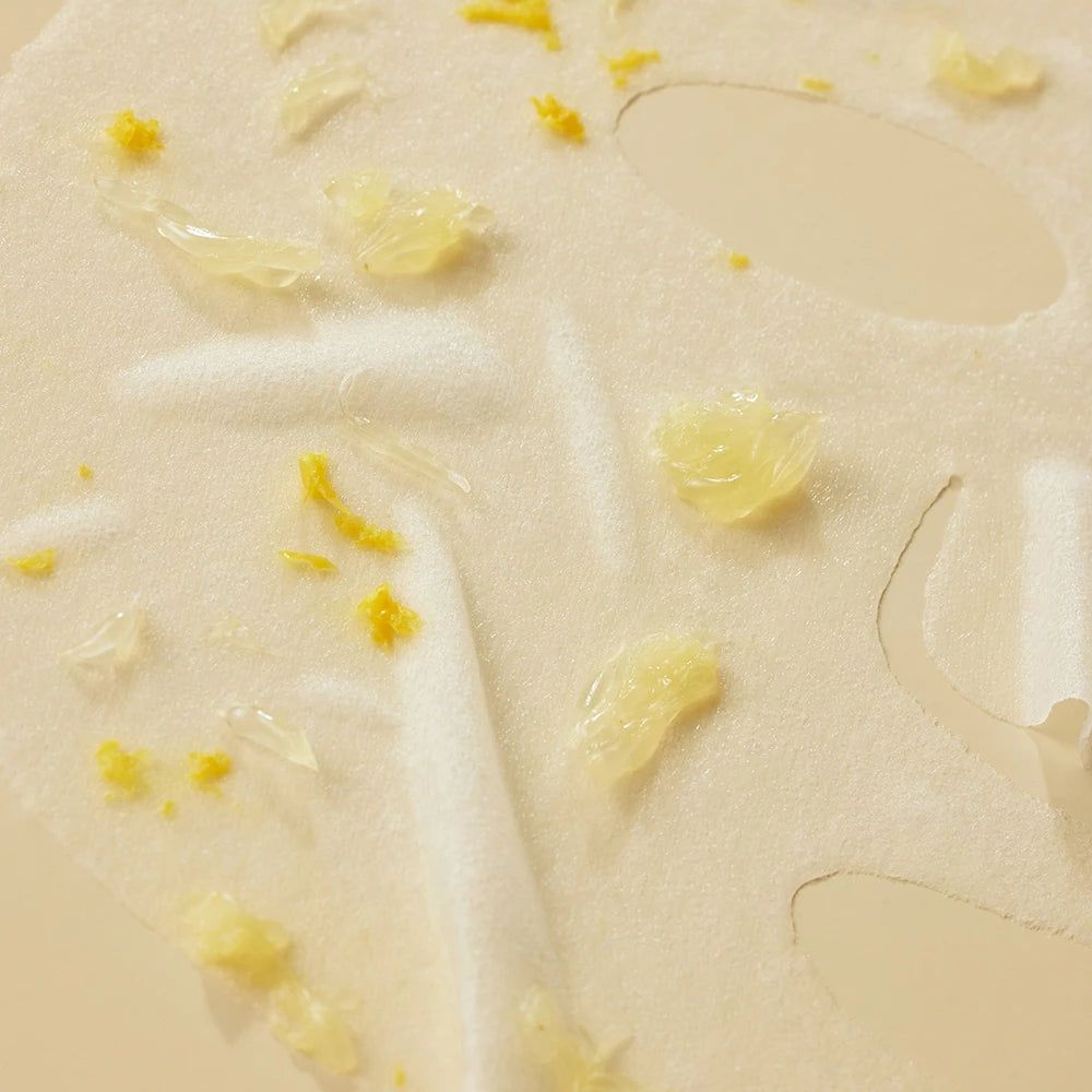 Gesichtsmaske mit gelben Partikeln. Die Maske hat Löcher für Augen und Mund. Nahaufnahme auf beigem Hintergrund.