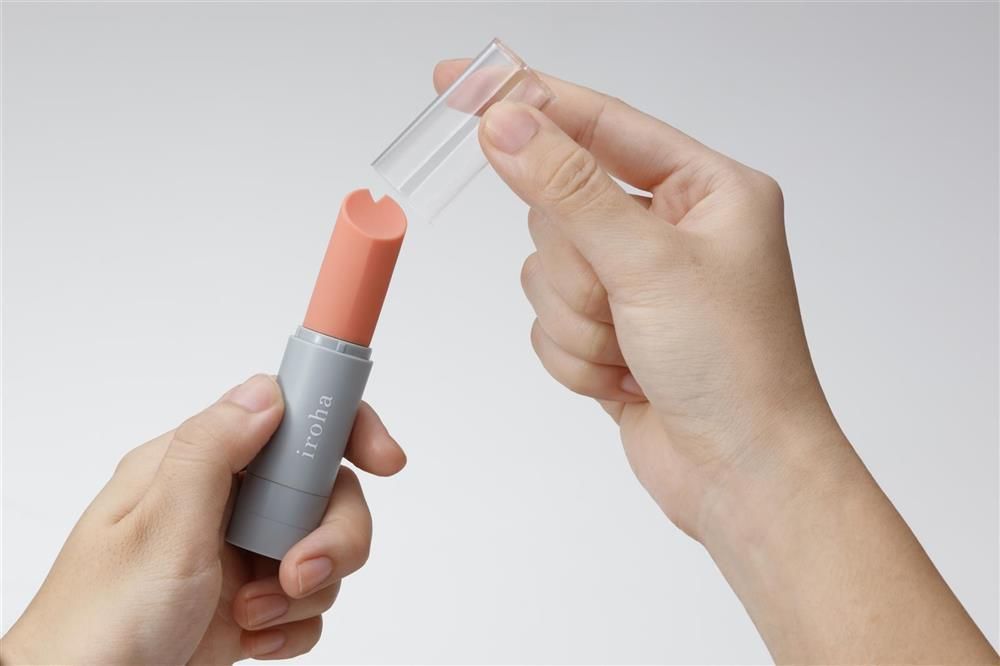 Hände halten einen grauen iroha STICK und eine transparente Kappe. Der Aufsatz ist korallenfarben.