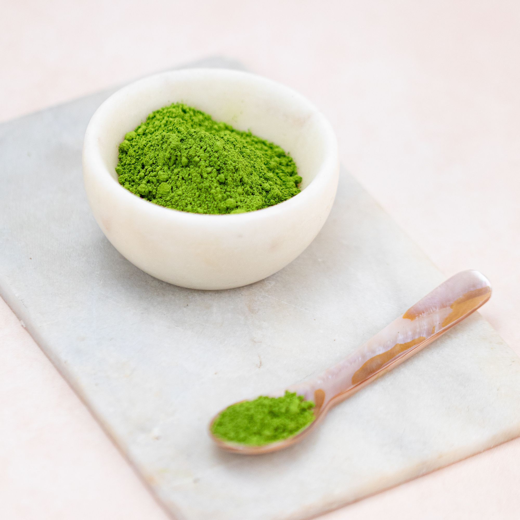 Schale mit Matcha-Pulver, Löffel mit Matcha auf Marmorplatte.