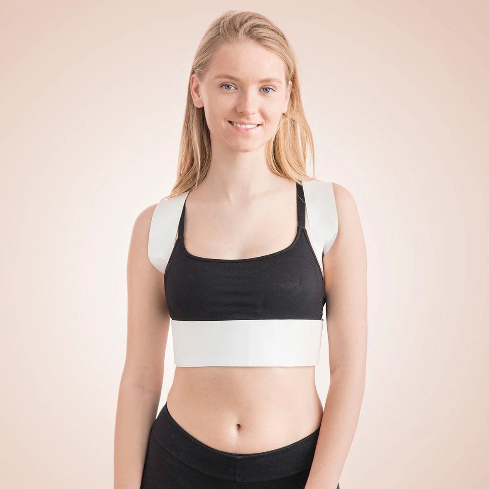 Person mit weißem Rückenkorrektor. Schwarzer Sport-BH. Schultergurte und Bauchgurt. Beige Hintergrund. Lächeln.