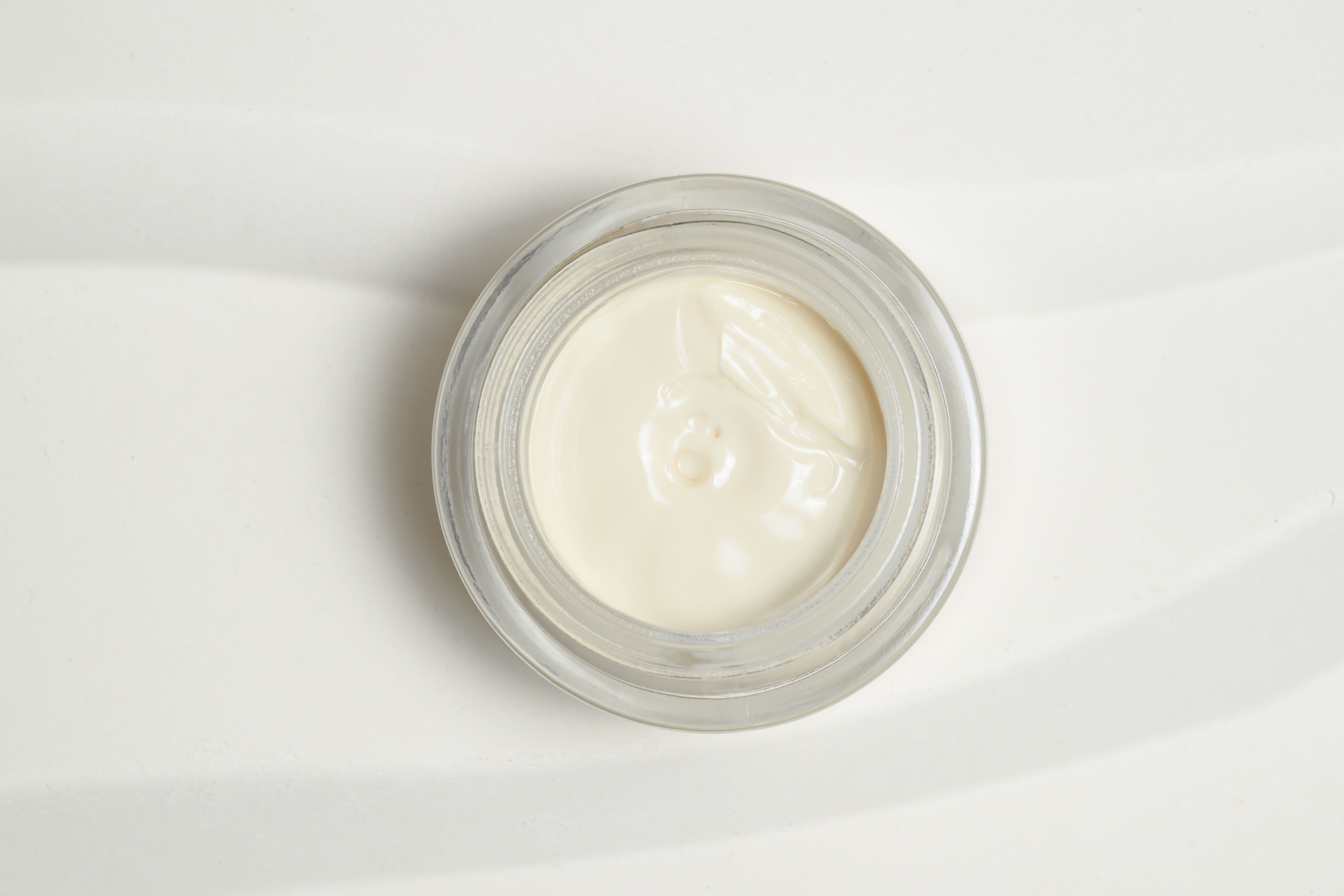 Creme in Glasbehälter, Draufsicht. Cremefarbene Creme. Transparenter Glasbehälter. Auf weißem Hintergrund.