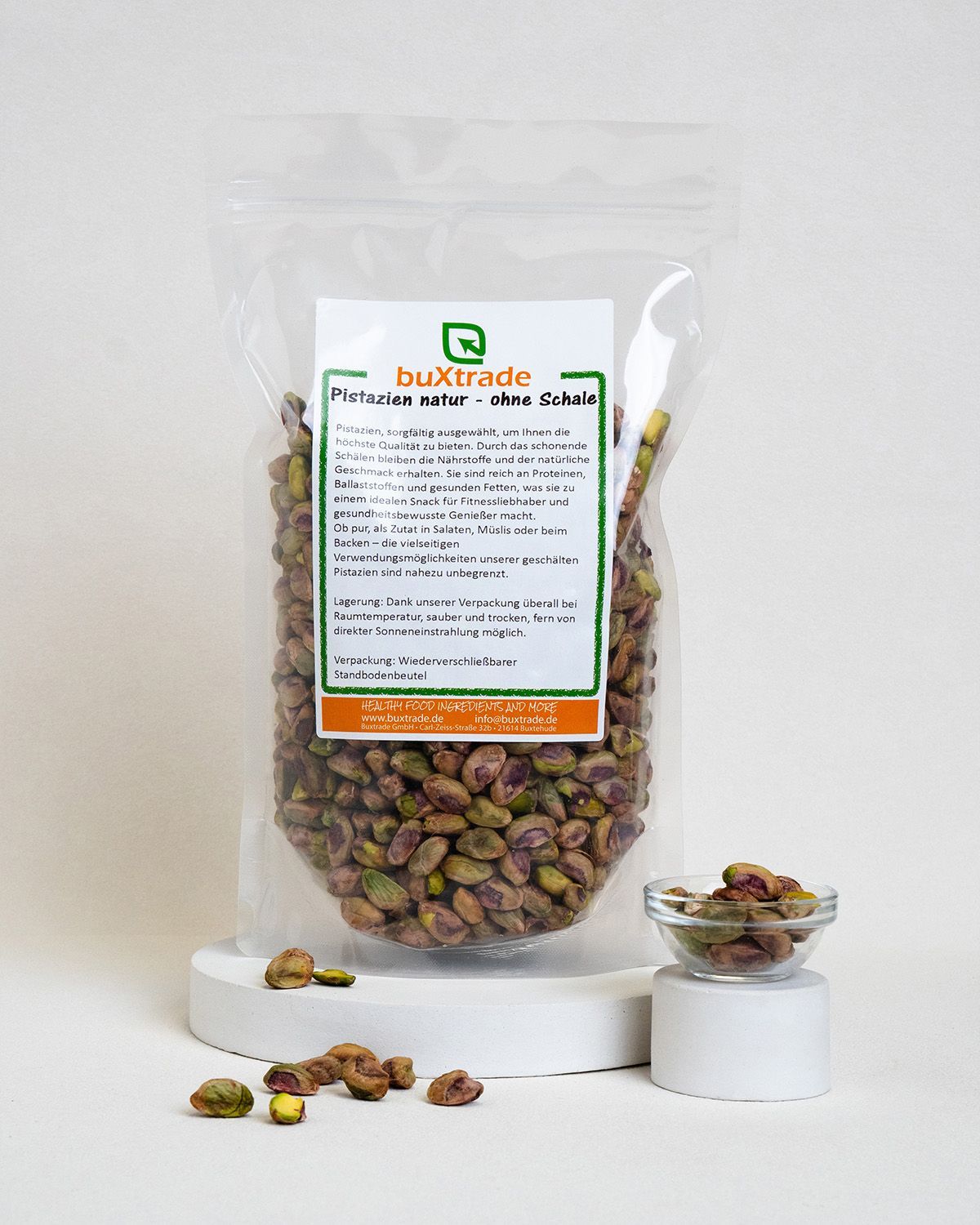 Verpackung mit Pistazienkernen auf Podest. Kleines Schälchen mit Kernen daneben. Etikett: buXtrade Pistazienkerne Natur ohne Schale.