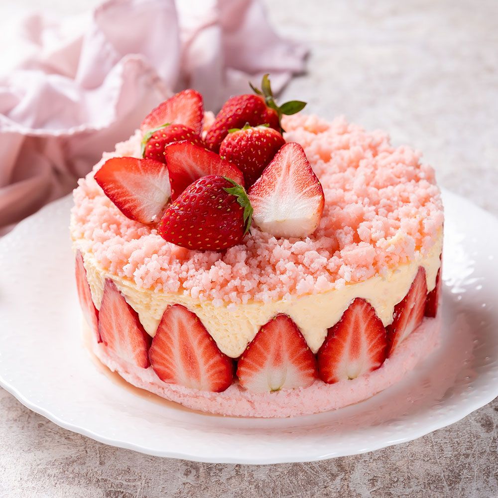 Torte mit Erdbeeren. Runde Torte mit Erdbeeren auf der Oberseite und am Rand. Rosa Krümel. Auf weißem Teller.