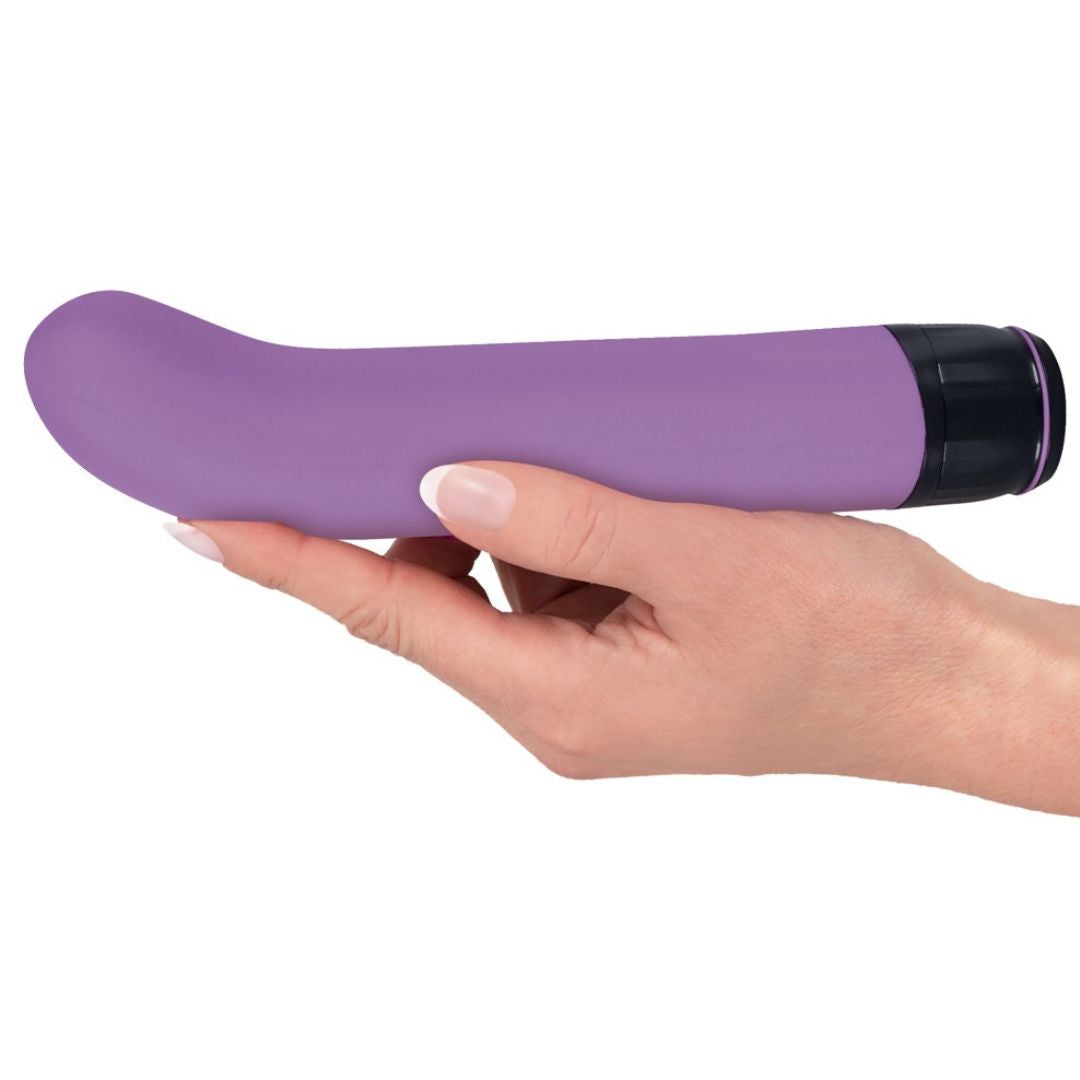 Lila Vibrator in Hand gehalten. Schwarzer Sockel. Gebogene Form.