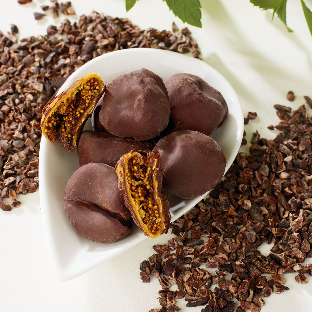 Schoko-Feigen in weißer Schale, umgeben von Kakaosplittern. Einige Feigen sind halbiert.