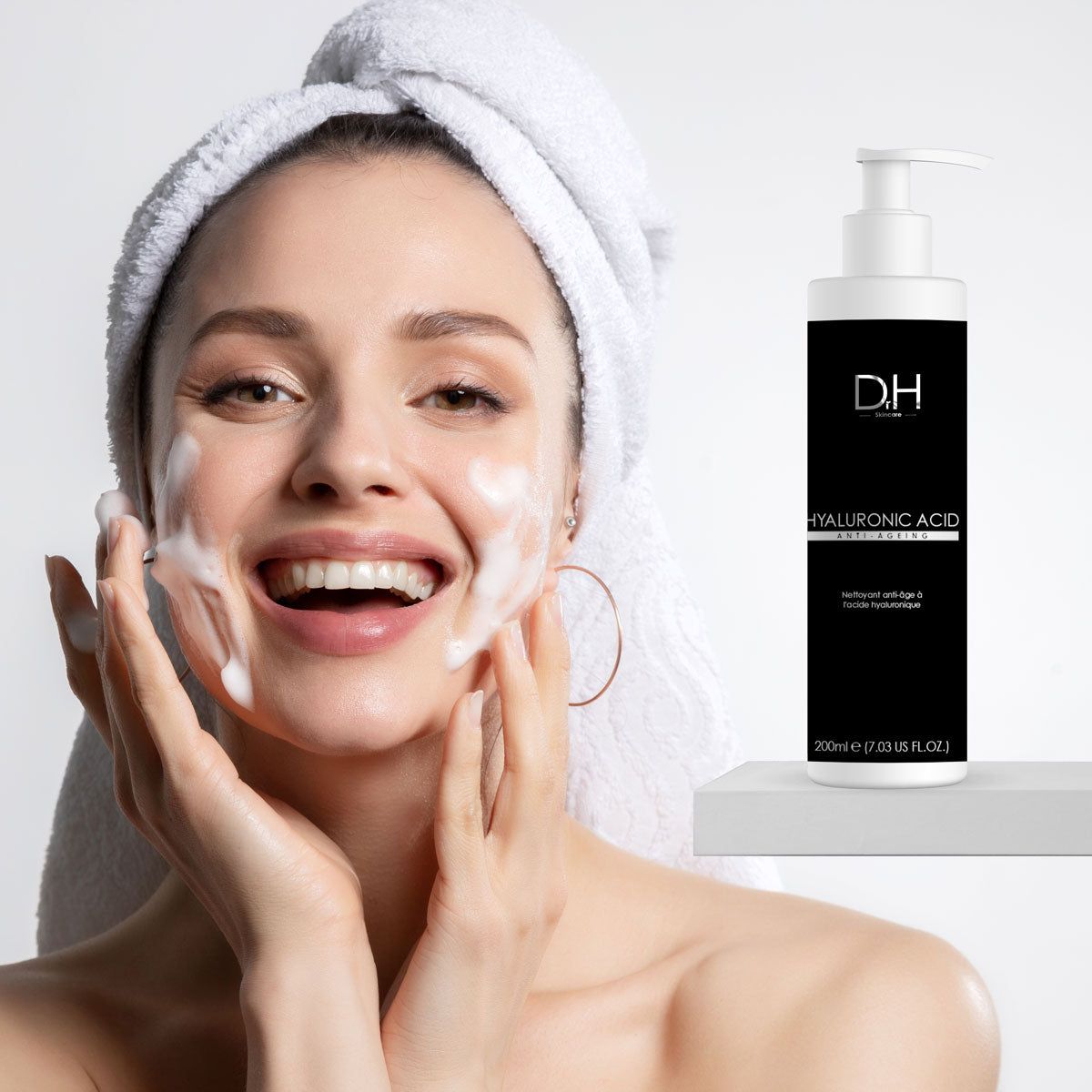 Frau mit Schaum im Gesicht und Handtuch. Flasche mit schwarzem Etikett. Aufschrift: HYALURONIC ACID, Anti-Aging. Mit Dosierpumpe.