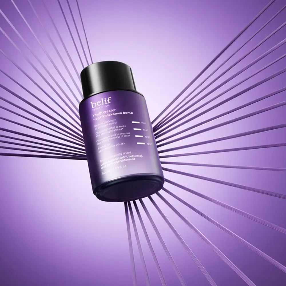 Lila Flasche mit schwarzem Deckel, umgeben von lila Linien. Aufschrift: belif, Youth creator - age knockdown bomb. Produkt auf lila Hintergrund.