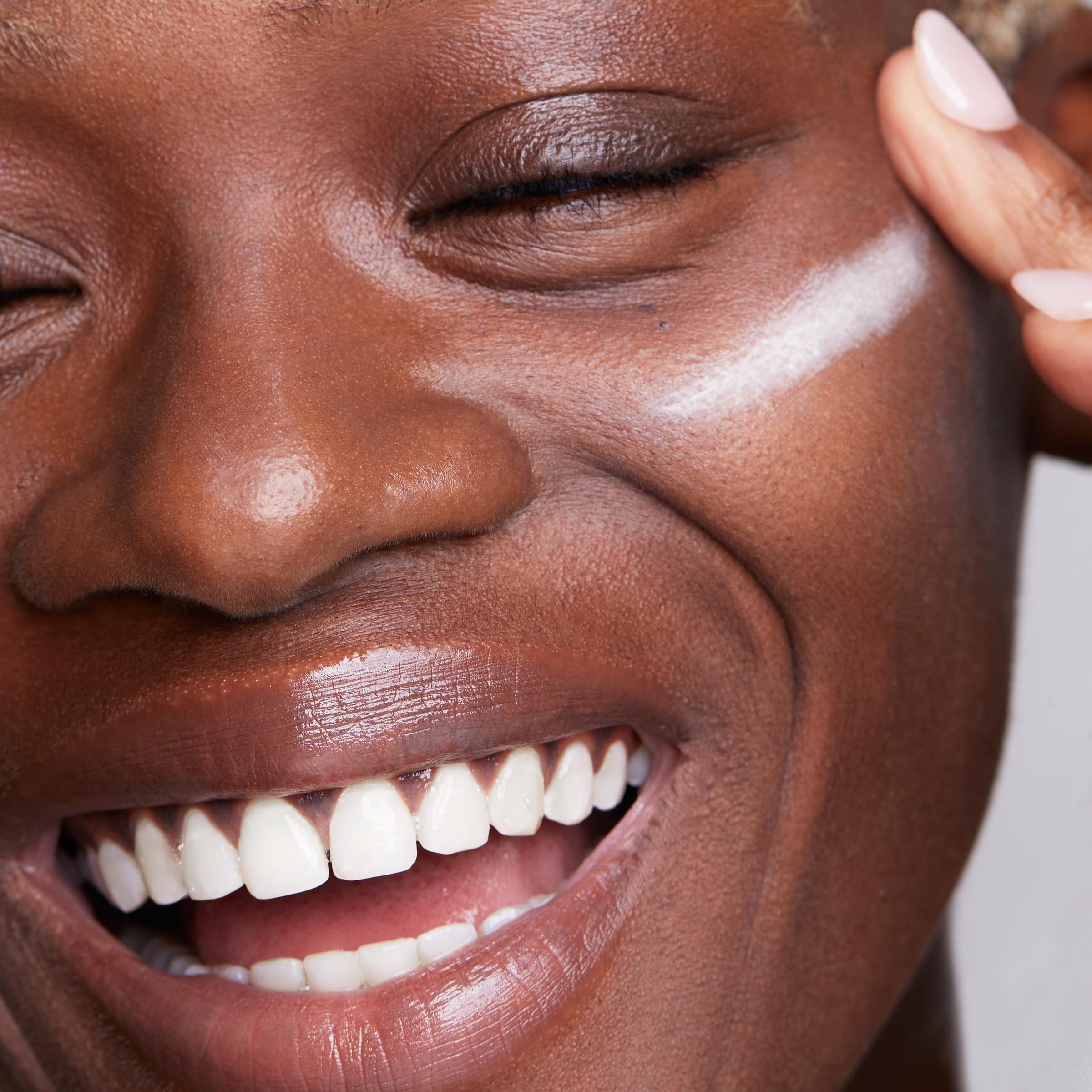 Nahaufnahme eines lächelnden Gesichts. Aufgetragenes Produkt auf der Wange.