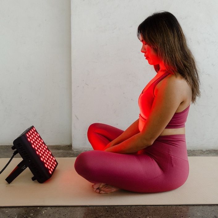 Frau sitzt im Schneidersitz mit Lichttherapiegerät. Gerät strahlt rotes Licht.