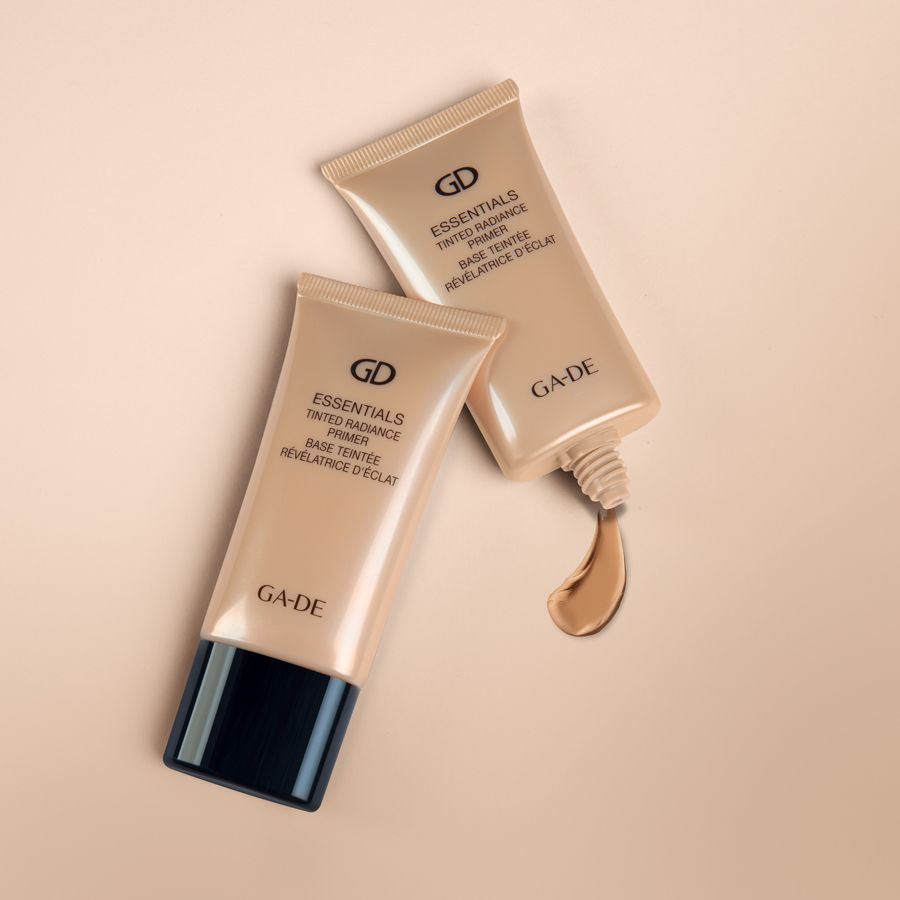 Zwei beige Tuben. Aufschrift: GD Essentials Tinted Radiance Primer. Marke: GA-DE. Produkt wird ausgegeben.