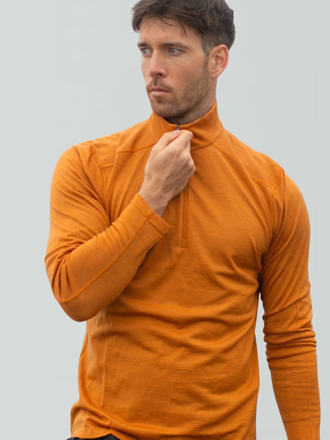 Mann trägt einen orangefarbenen Merino-Pullover mit Reißverschluss und langen Ärmeln.
