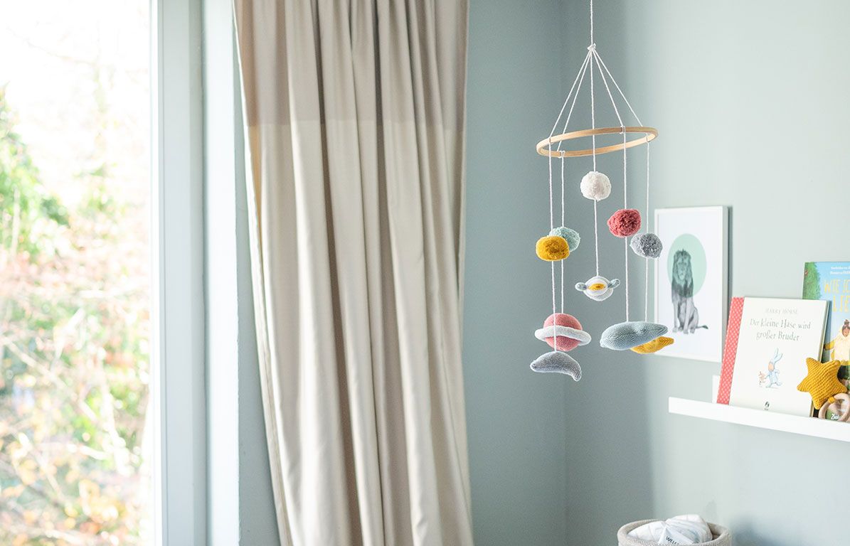 Mobile über einem Kinderbett. Holzring mit bunten Elementen: Kugeln, Sterne und Planeten. In einem Zimmer.