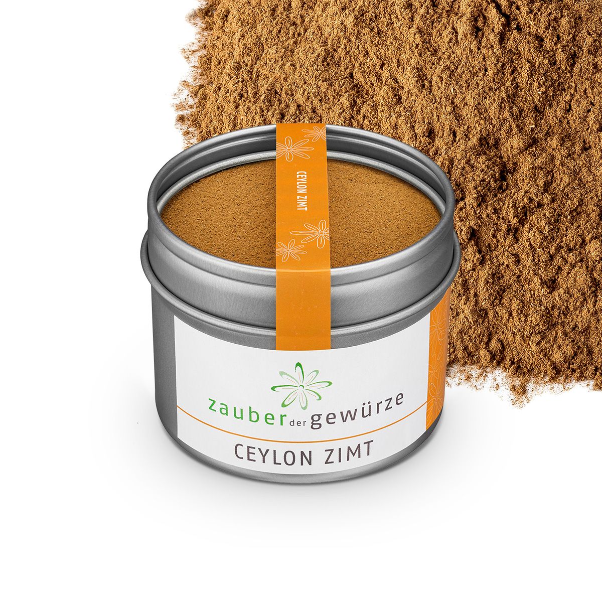 Runde Dose mit gemahlenem Zimt und Zimtpulver daneben. Orangefarbener Aufkleber mit Text: Ceylon Zimt. Weißes Etikett mit Text: Zauber der Gewürze, Ceylon Zimt.