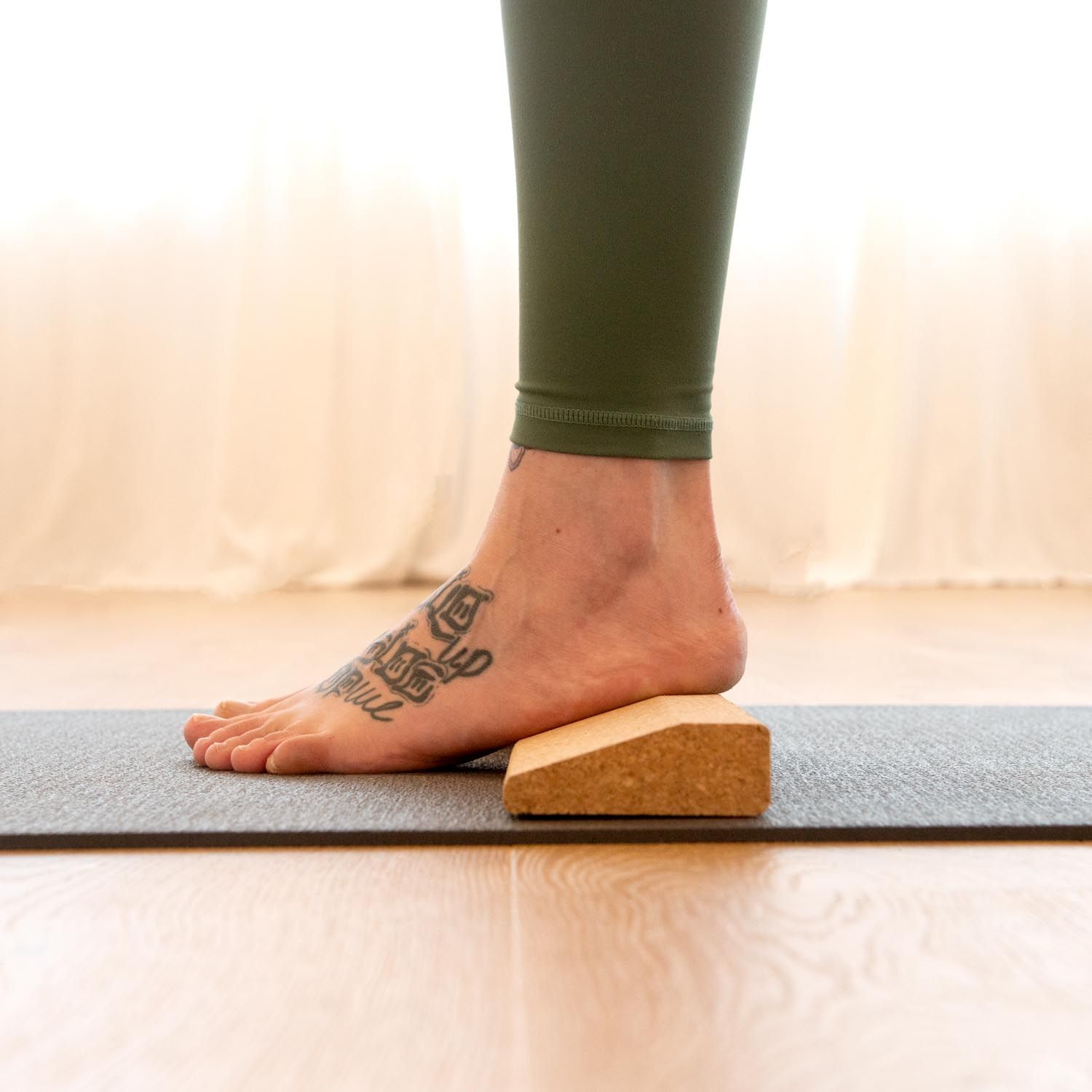 Fuß auf der Kork-Handstandplanke auf einer Yogamatte. Bein mit Tätowierung. Braune Farbe.