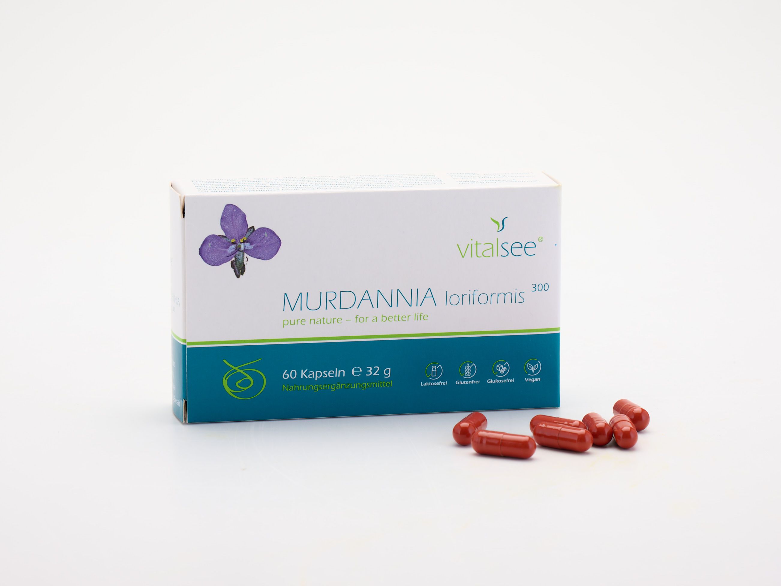 Weiße Schachtel mit lila Blüte und Text. Daneben liegen rote Kapseln. Aufschrift: Vitalsee, MURDANNIA loriformis 300 Extrakt.