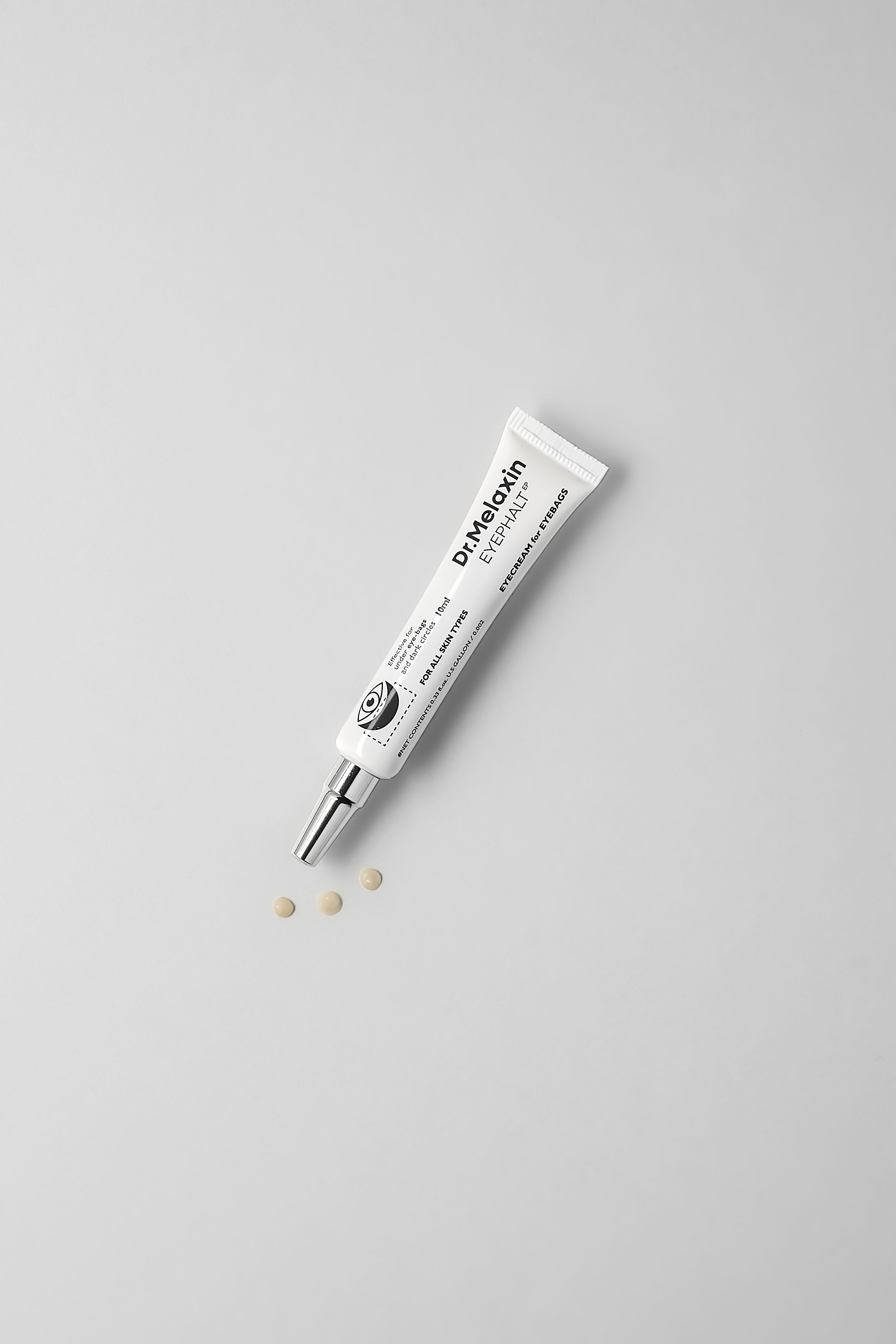 Weiße Tube mit silberner Spitze. Aufschrift: Dr.Melaxin EYEPHALT EYE CREAM for EYEBAGS. 10ml. Für alle Hauttypen. Drei Tabletten daneben.