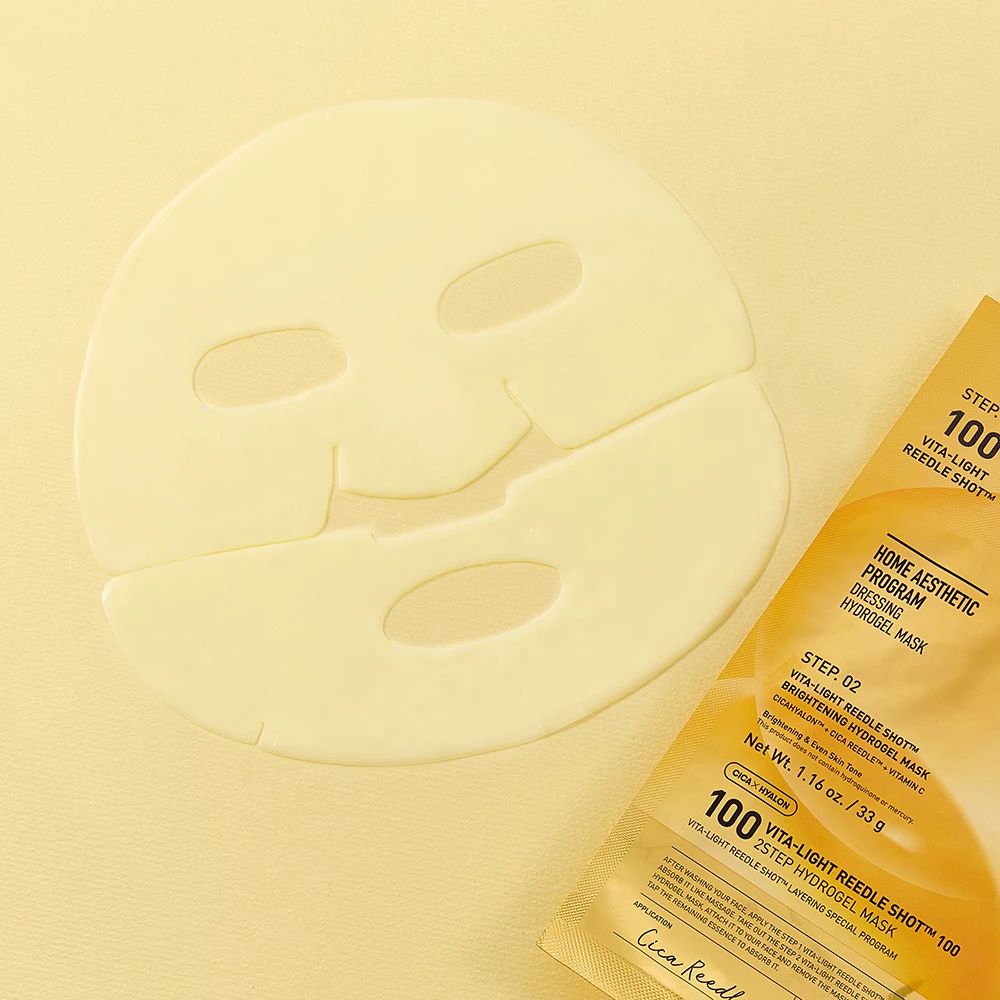 Ein hellgelber Hydrogel-Gesichtsmasken-Bogen mit Augen-, Nasen- und Mundöffnungen liegt neben einer passenden Verpackung.