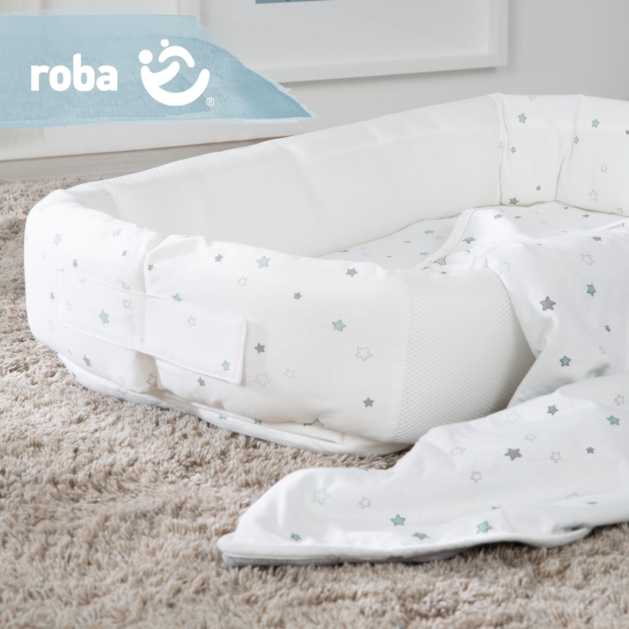 Weiße Babylounge und Decke mit Sternenmuster. Die Babylounge hat einen Griff. Das Logo von roba ist sichtbar.