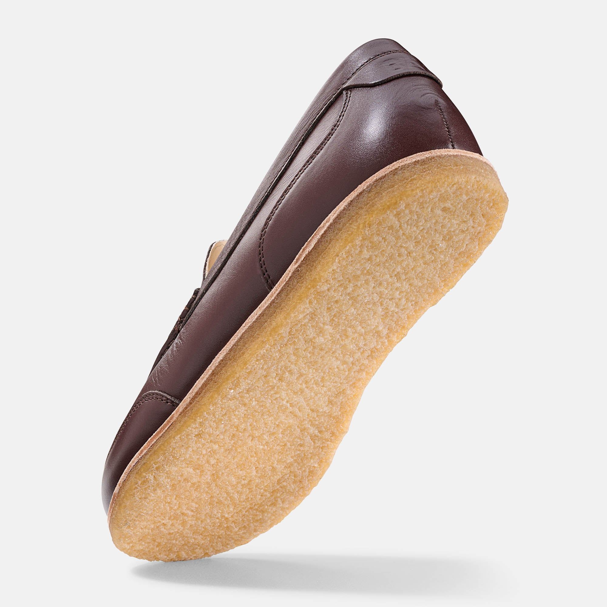 Brauner Leder-Slipper, schräg von unten. Helle Sohle, sichtbare Nähte. Klassisches Design.