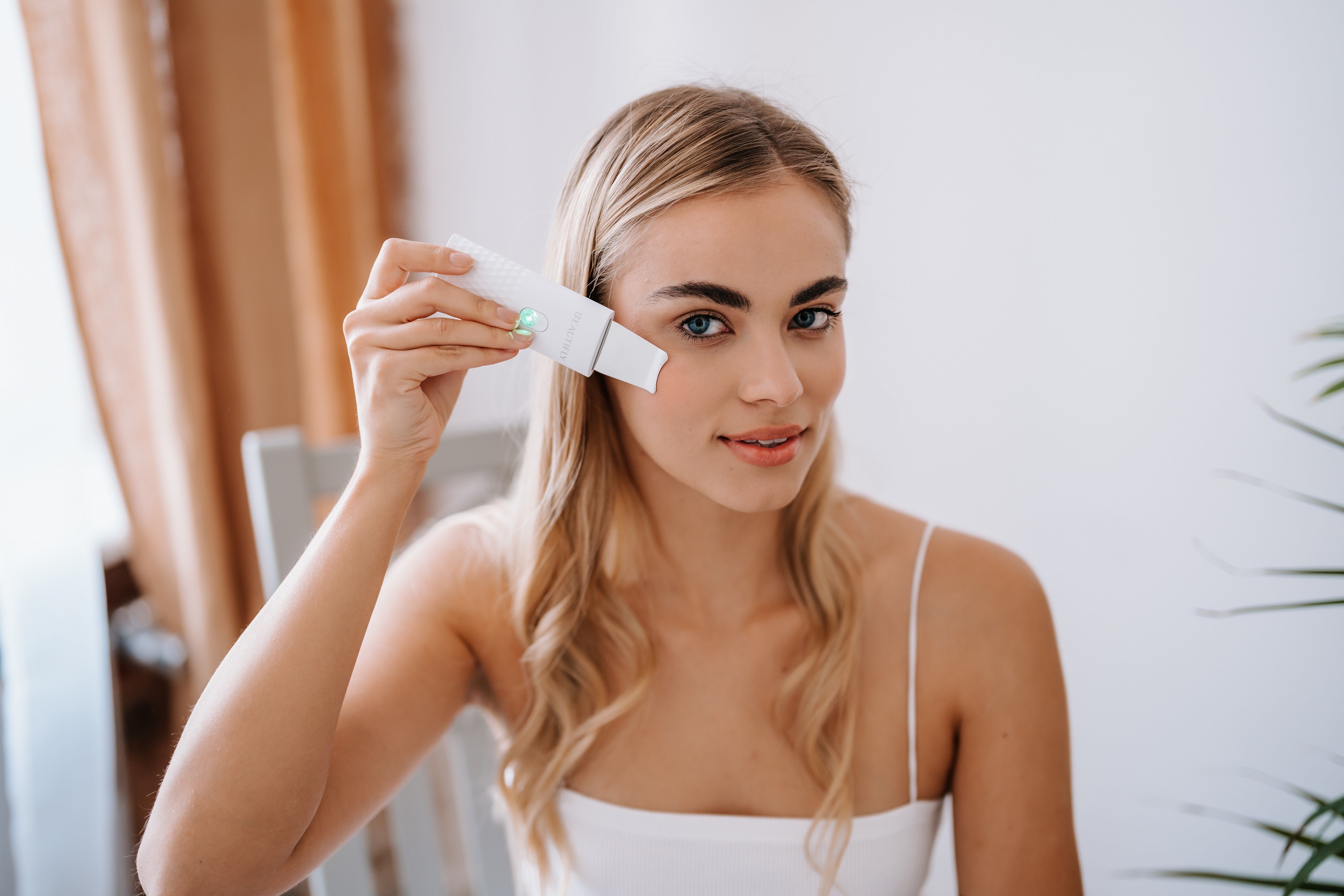 Frau hält BEAUTIFLY B-Scrub Mini an Gesicht. Gerät weiß, mit silberner Spitze. Frau trägt Top.