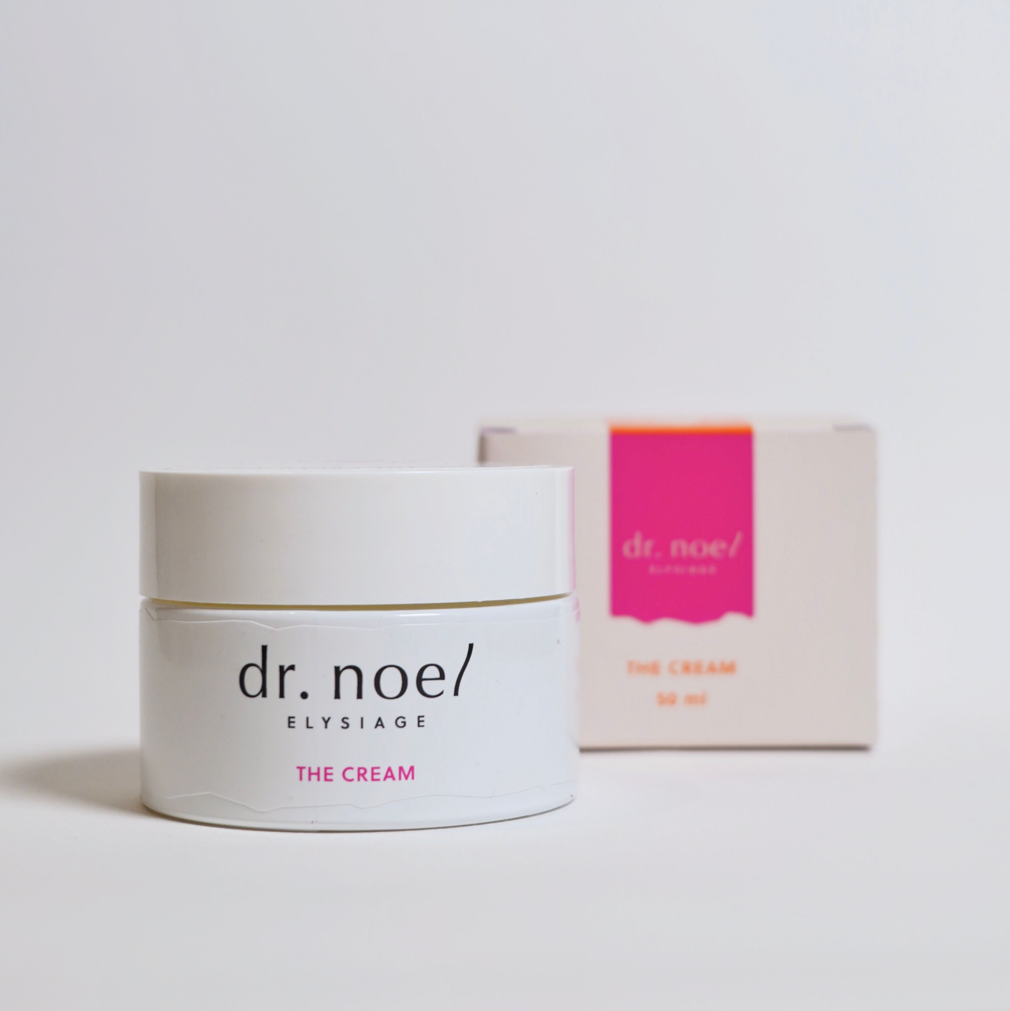 Weißes Creme-Glas mit Aufschrift 'dr. noel/ ELYSIAGE THE CREAM' und rosa Box.