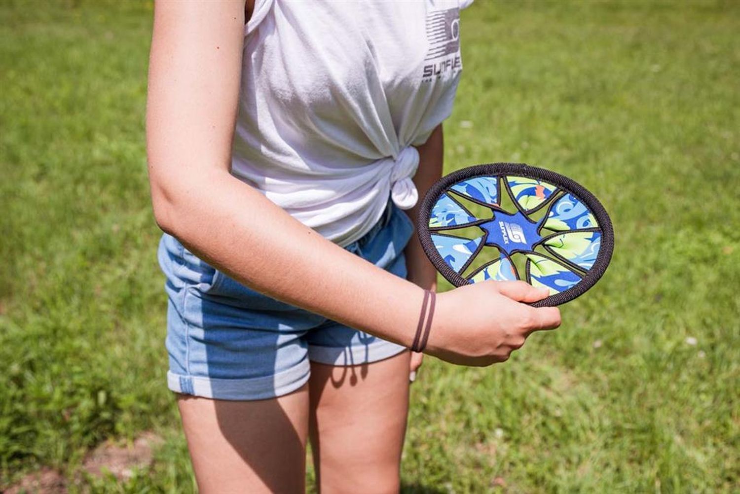 Person hält einen blauen Frisbee mit floralem Muster. Grasiger Hintergrund.