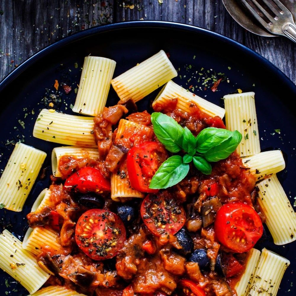 Pasta mit Tomatensauce, Oliven und Basilikum. Blaue Platte. Nahaufnahme.