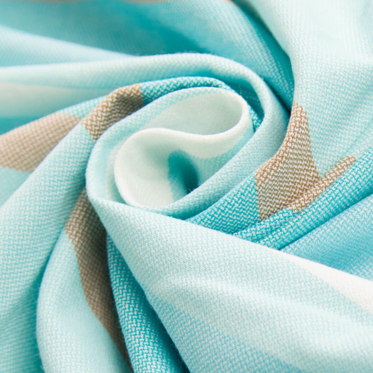 Nahaufnahme eines gefalteten Babytragetuchs mit blau-, beige- und weißen Streifen. Stoffstruktur sichtbar.