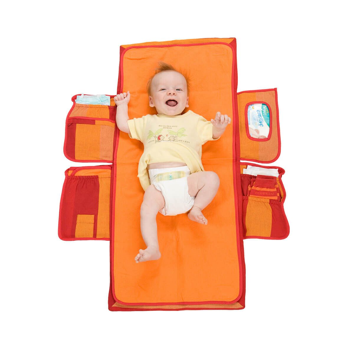 Wickelmax Windeltaschen Organizer, offen. Orange mit roten Akzenten. Baby liegt darauf. Mehrere Taschen für Zubehör.