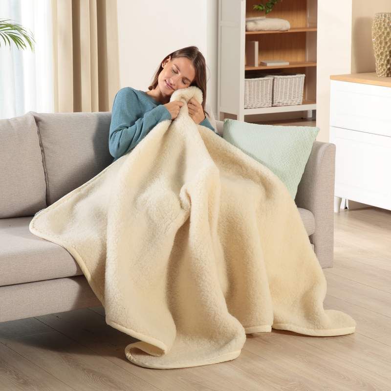 Frau umarmt beige Schurwolldecke. Weiche Textur, rechteckige Form. Auf Sofa sitzend.